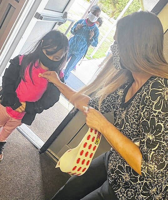 
			
				                                Teachers across the Public Schools of Robeson County are facing challenges including burnout as a result of the pandemic and staffing shortages. Pictured is R.B. Dean-Townsend Elementary School Teacher Assistant Donna Hager placing stickers on students as they enter a school building on March 1, 2021. The stickers were given to students each day after staff members checked their temperatures.
 
			
		
