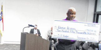 
			
				                                David Powell, director of the Robeson County Offender Resource Center, displays a check Monday during a meeting of the Robeson County Board of Commissioners that denotes $250,000 in state funding coming to the inmate reentry program.
 
			
		