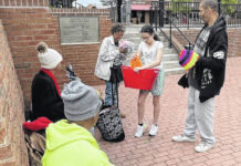 
			
				                                Jazlyn Jacobs, center, passes out handmade caps to group of people who had gathered at Lumberton’s downtown plaza Saturday. 
                                 Michael Futch | Robesonian

			
		